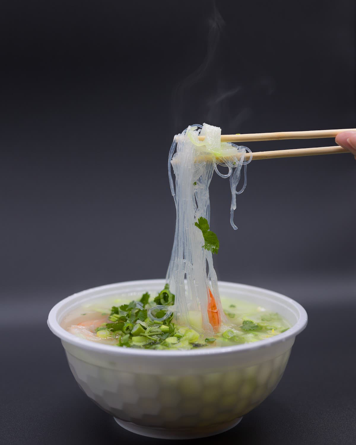 Chopsticks lifting noodles from a white bowl with greens